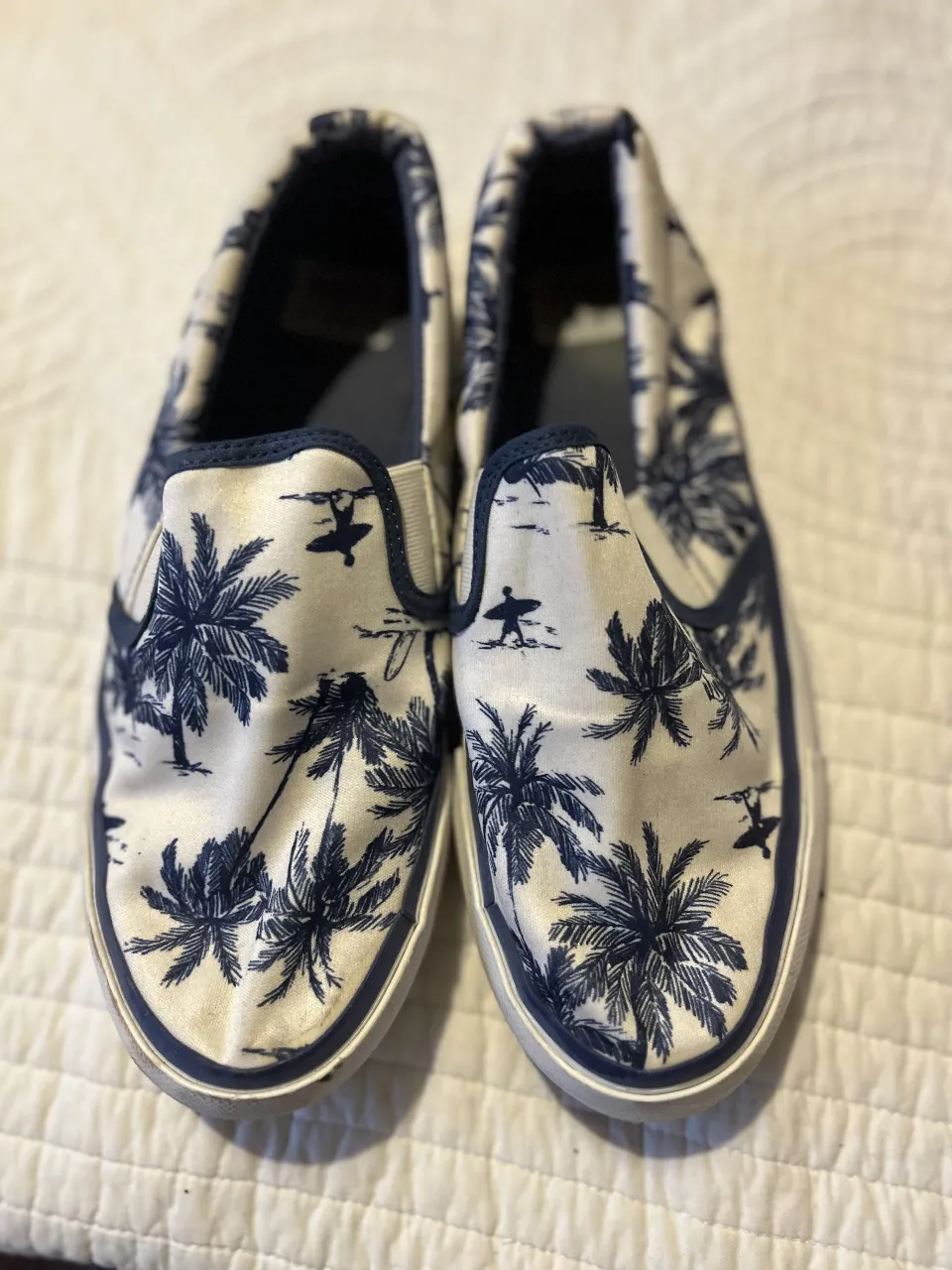 Zapatillas slip-on con estampado de palmeras en blanco y azul marino. Marca Mimo & Co, ideales para un look casual y playero.