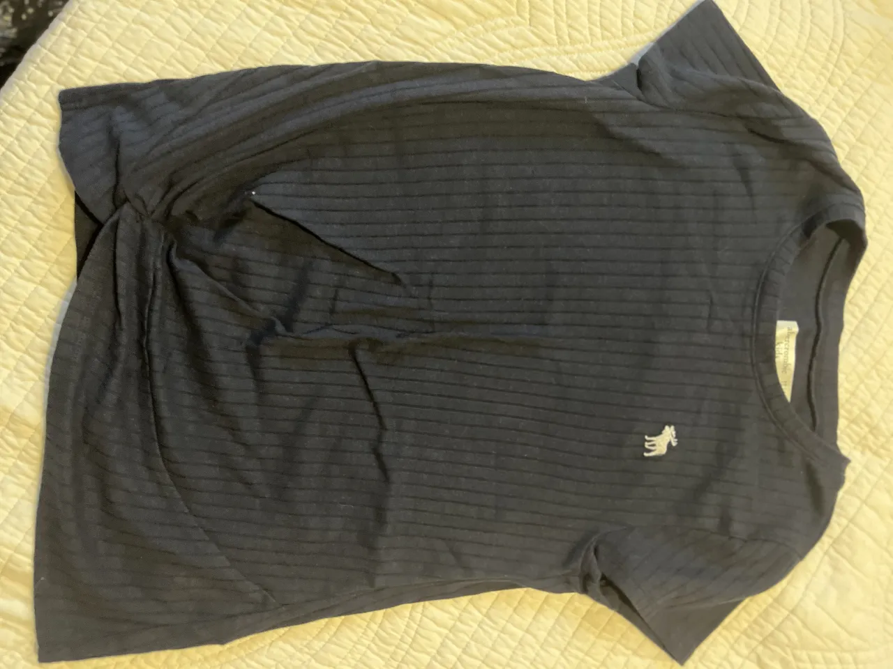 Remera de manga corta para niña, de la marca Abercrombie Kids. Confeccionada en tejido de punto acanalado de color azul marino. Presenta un detalle de logo bordado en el pecho. Ideal para un look casual y cómodo.