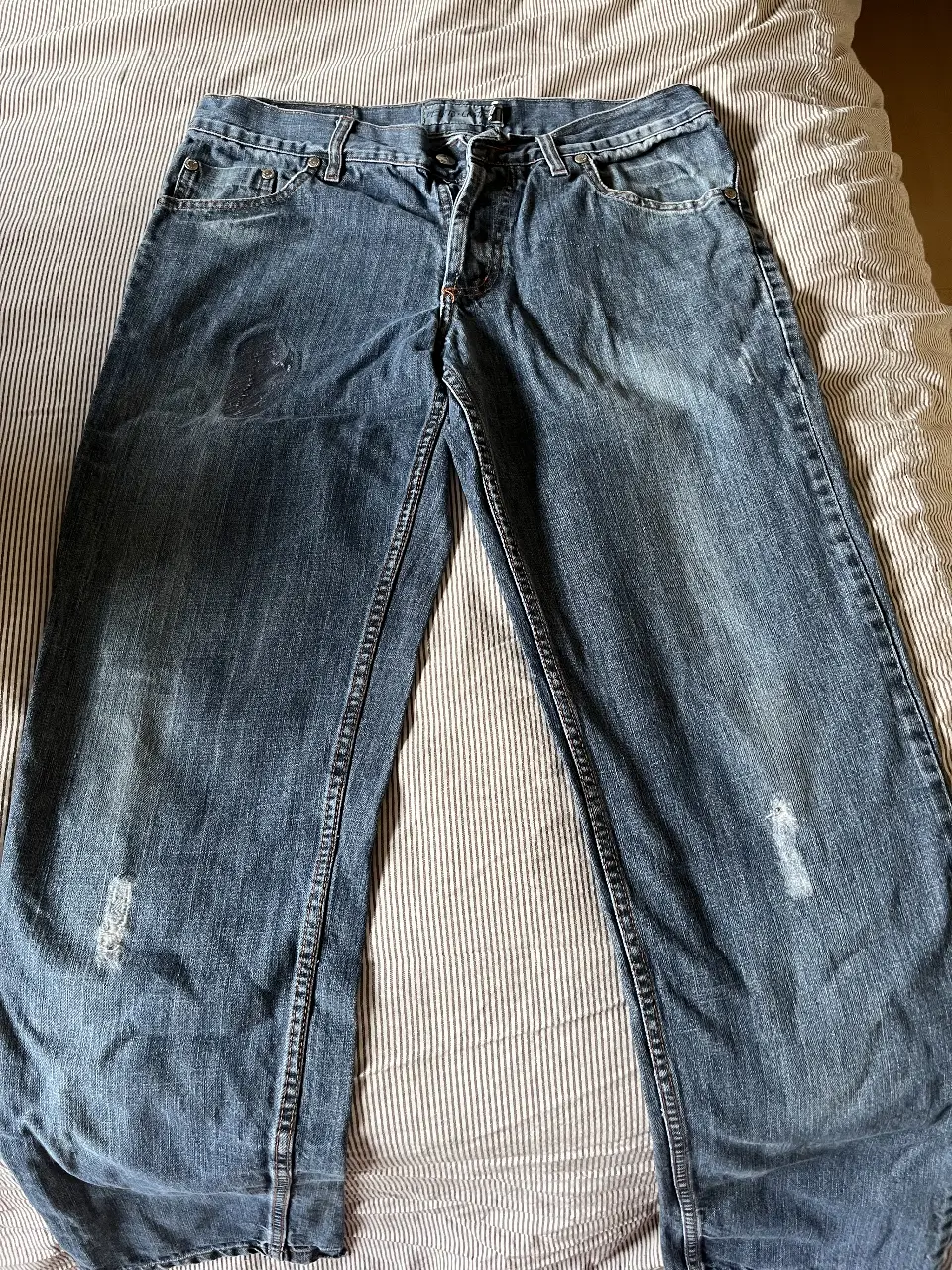 Jeans de hombre, azul gastado con roturas en las rodillas. Tiro medio, corte recto y estilo casual. Perfecto para un look urbano y relajado.