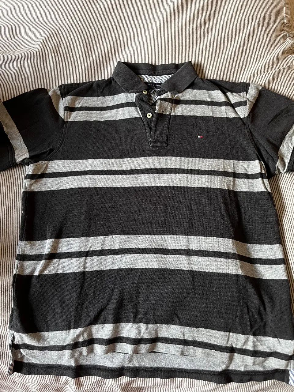 Remera polo de hombre Tommy Hilfiger a rayas horizontales en negro y gris. Confeccionada en algodón, ideal para un look casual y cómodo. Talle M.