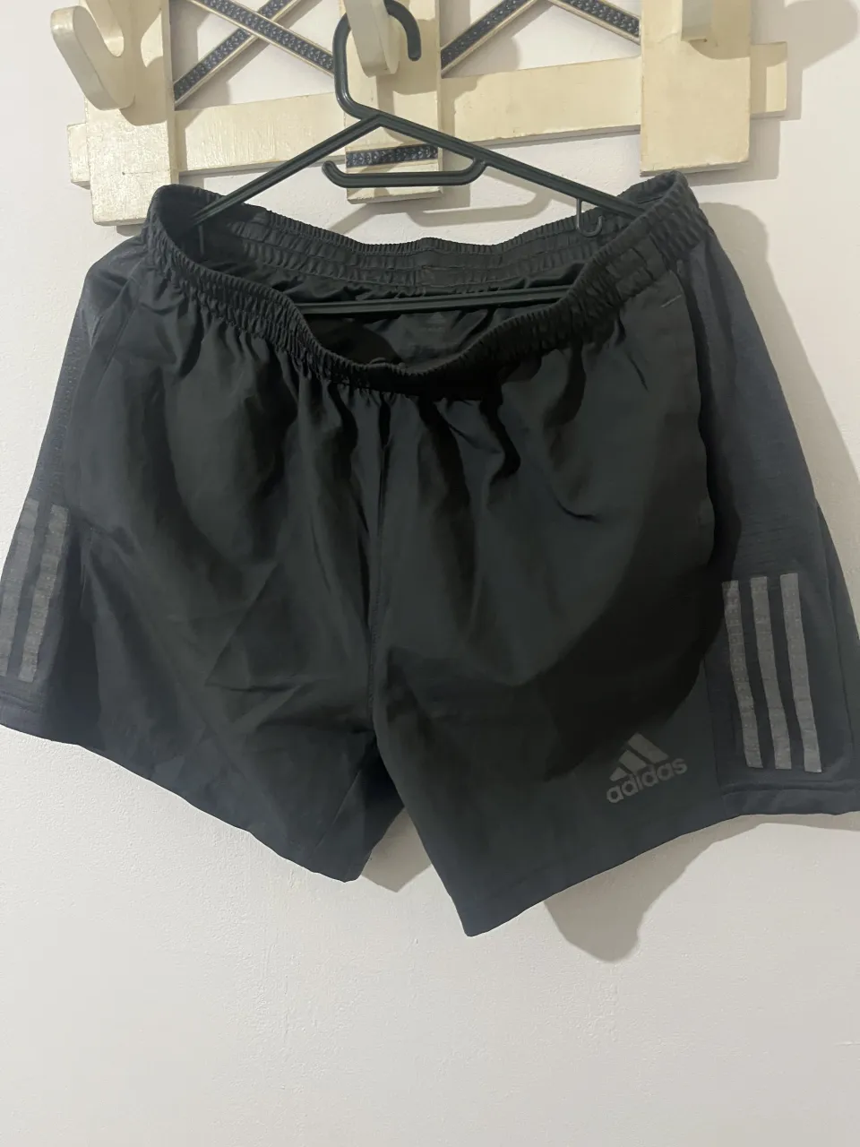 Shorts deportivos gris de running con tres franjas grises reflectivas en los laterales y logo de la marca. Posee 2 bolsillos laterales y uno en la parte trasera con cierre.