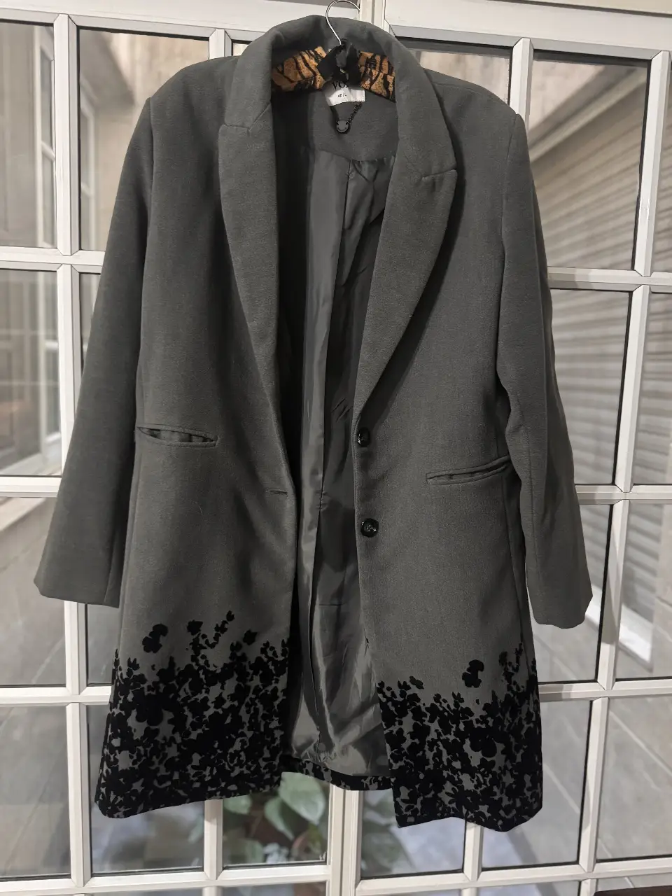 Elegante blazer gris con detalles florales en negro en el borde inferior. Ideal para un look sofisticado y moderno.