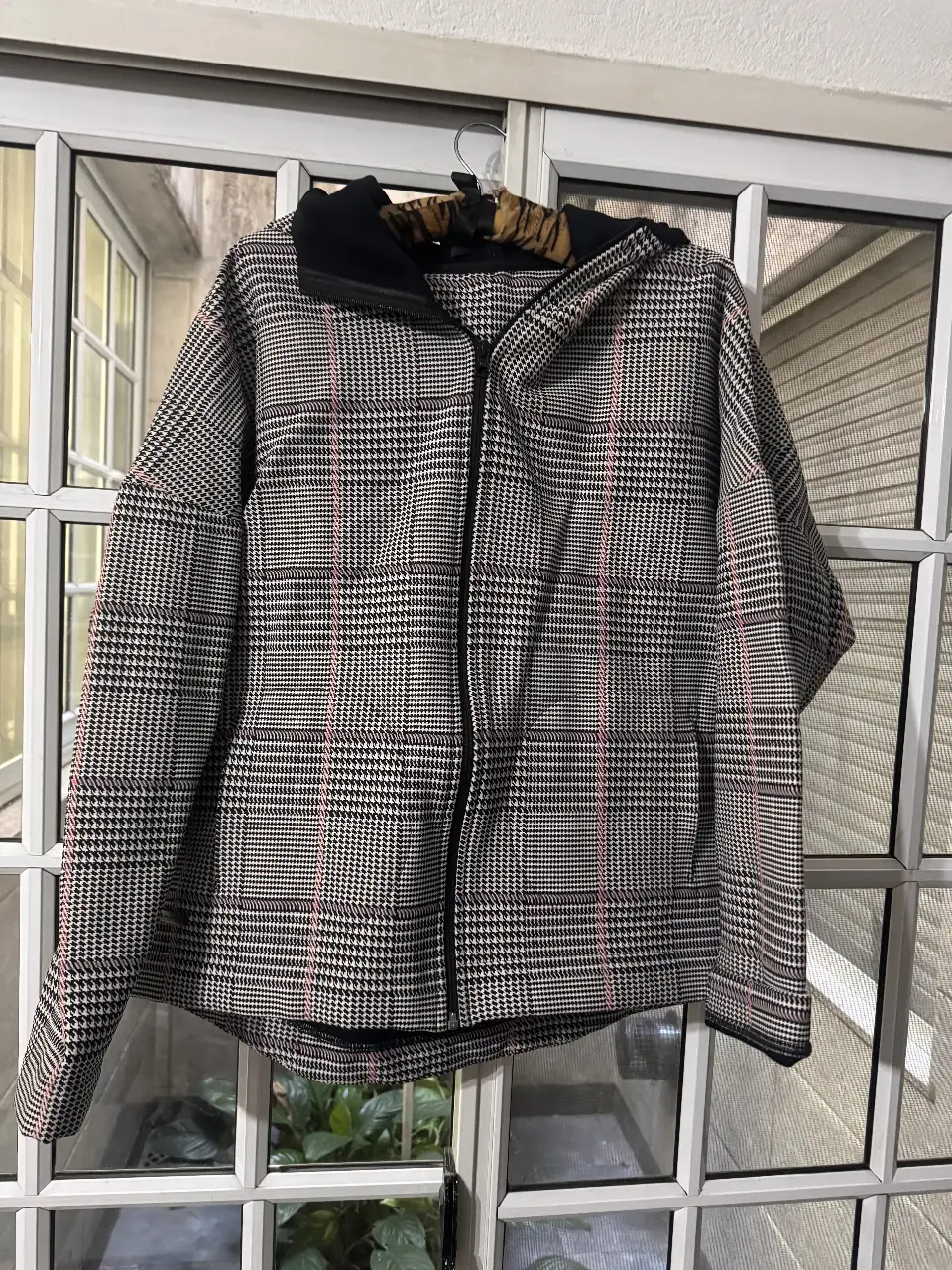 Campera con capucha de tela escocesa en tonos grises y negros con detalles en rosa. Posee cierre frontal y etiqueta de la marca Punto 1. Ideal para un look casual y abrigado.