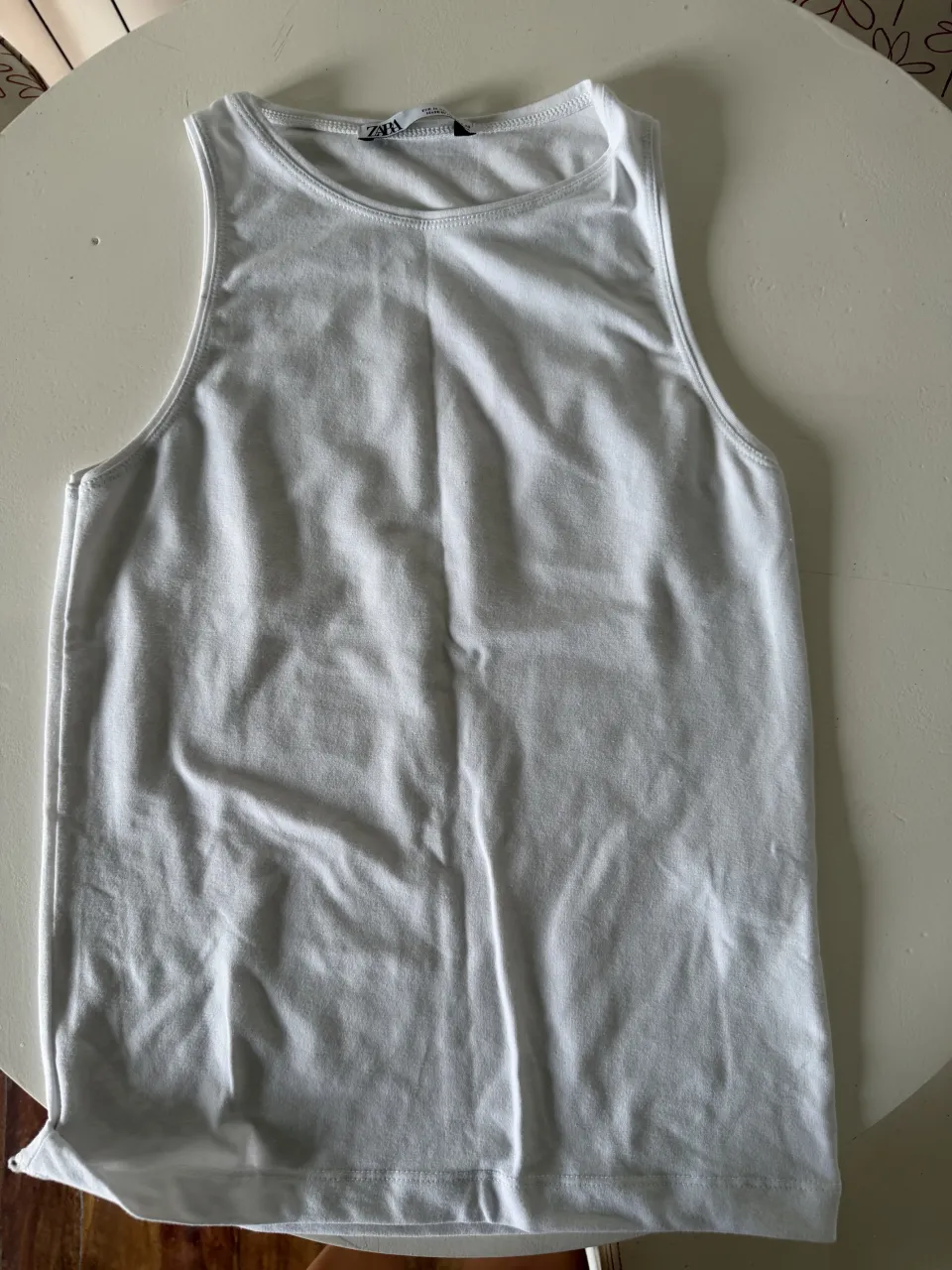 Musculosa blanca básica de Zara, ideal para el día a día o para combinar con otras prendas. Su diseño liso y corte clásico la hacen súper versátil.