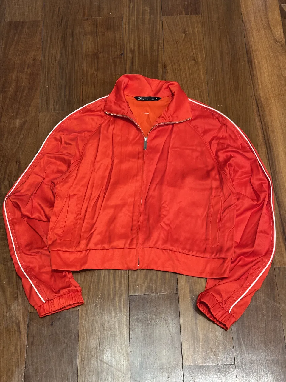 Campera deportiva roja, tiro corto, con detalles blancos en los laterales de las mangas y cuello. Ideal para un look urbano y canchero.