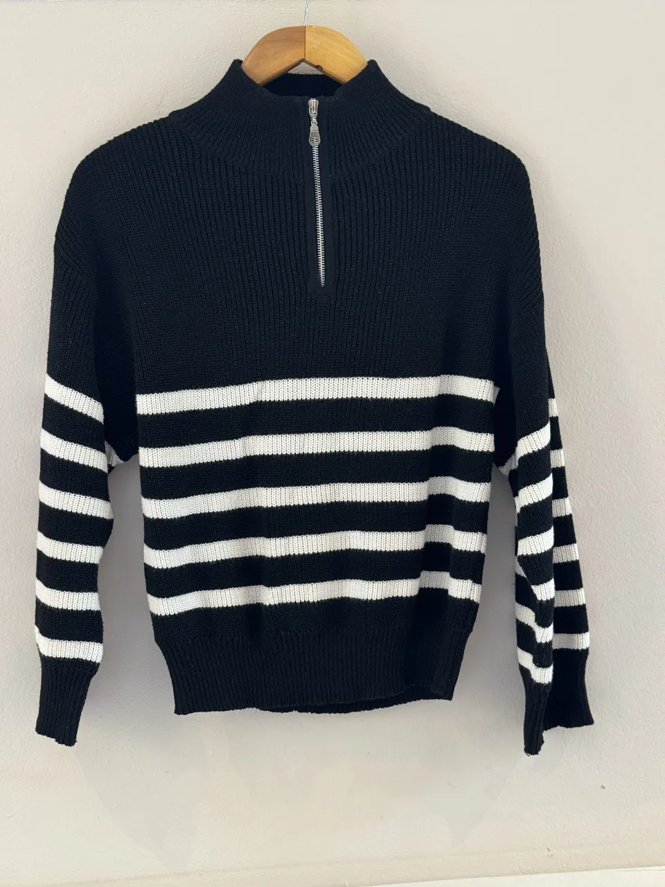 Sweater de lana negro con rayas blancas horizontales. Cuello alto con cierre metálico plateado. Ideal para un look casual y cómodo.
