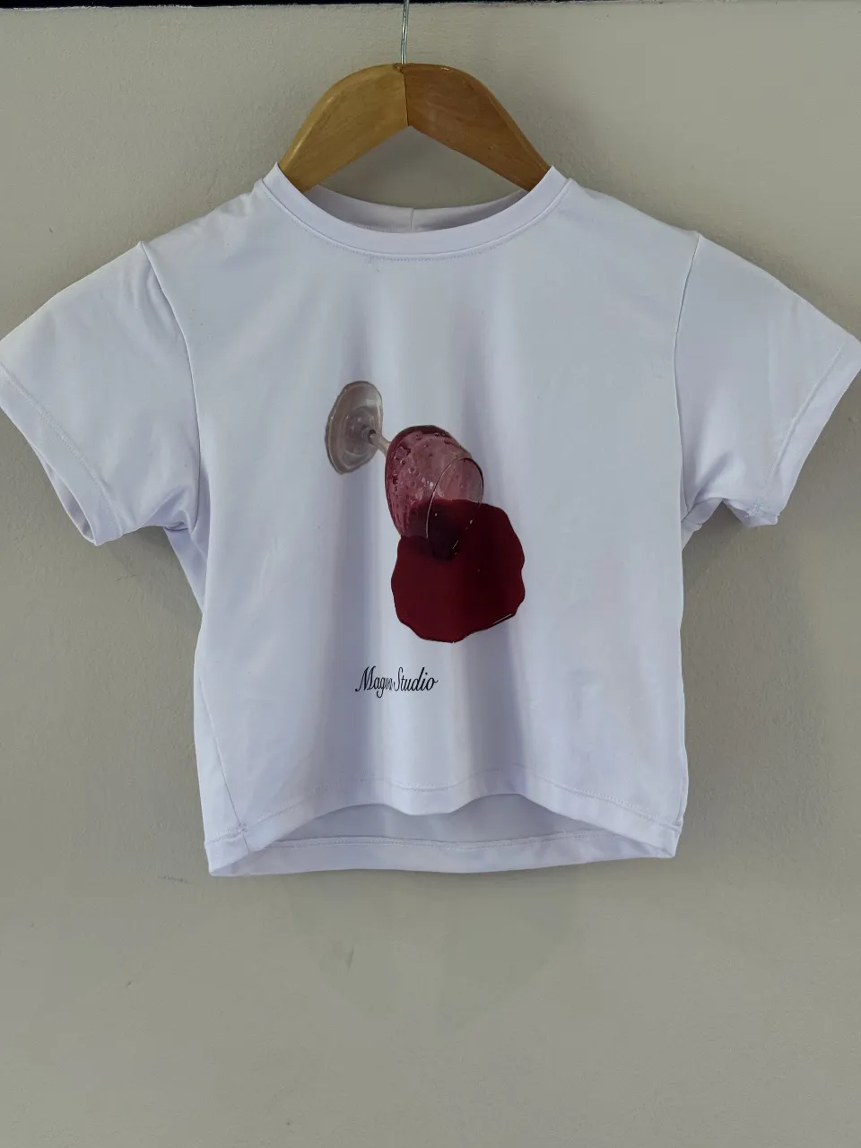 Remera blanca crop con estampa de copa de vino tinto derramada y el logo 'Magva Studio'.