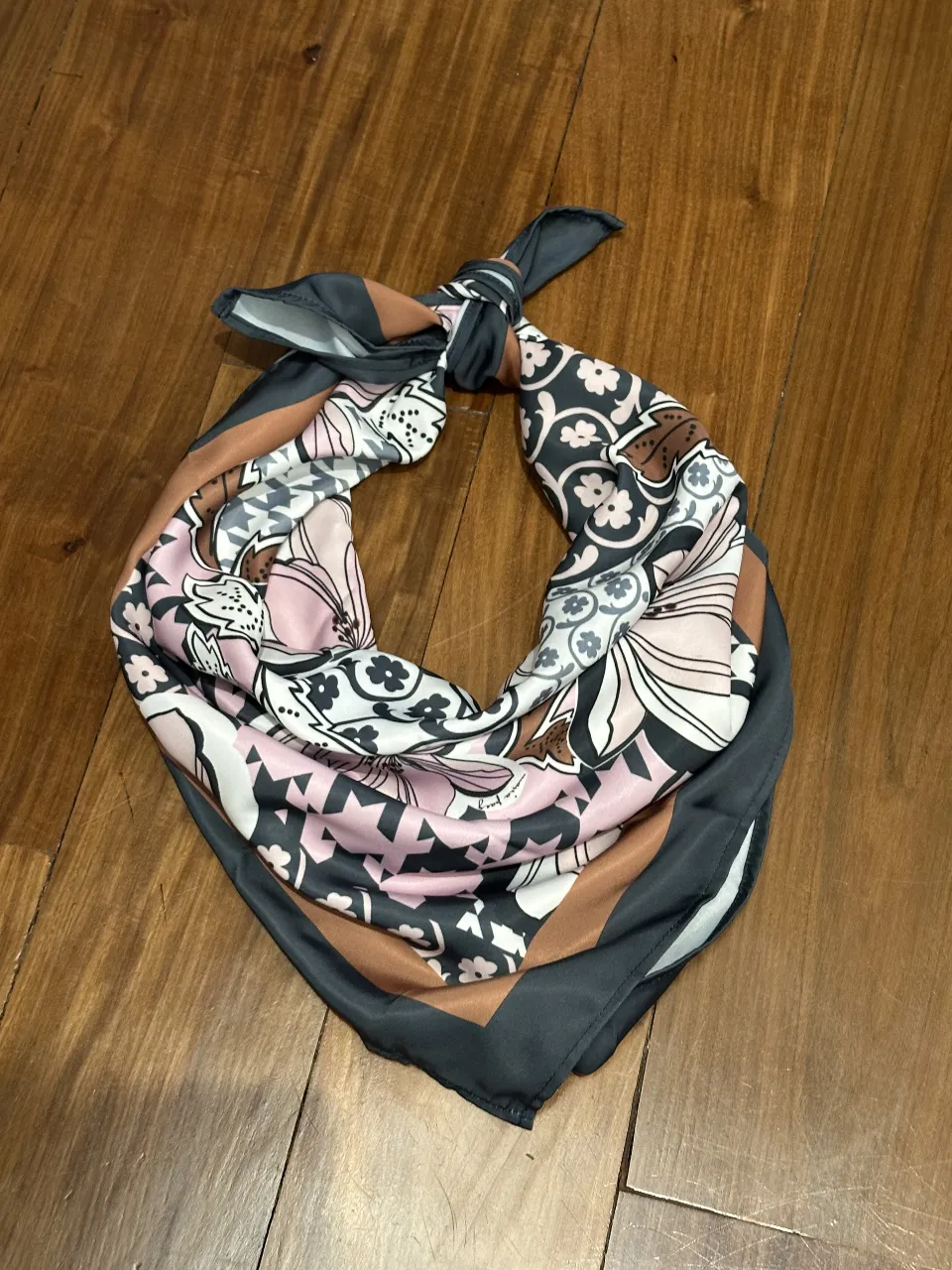 Pañuelo de seda con estampado floral y motivos geométricos en tonos rosa, gris, marrón y blanco. Ideal para darle un toque chic a tu outfit.