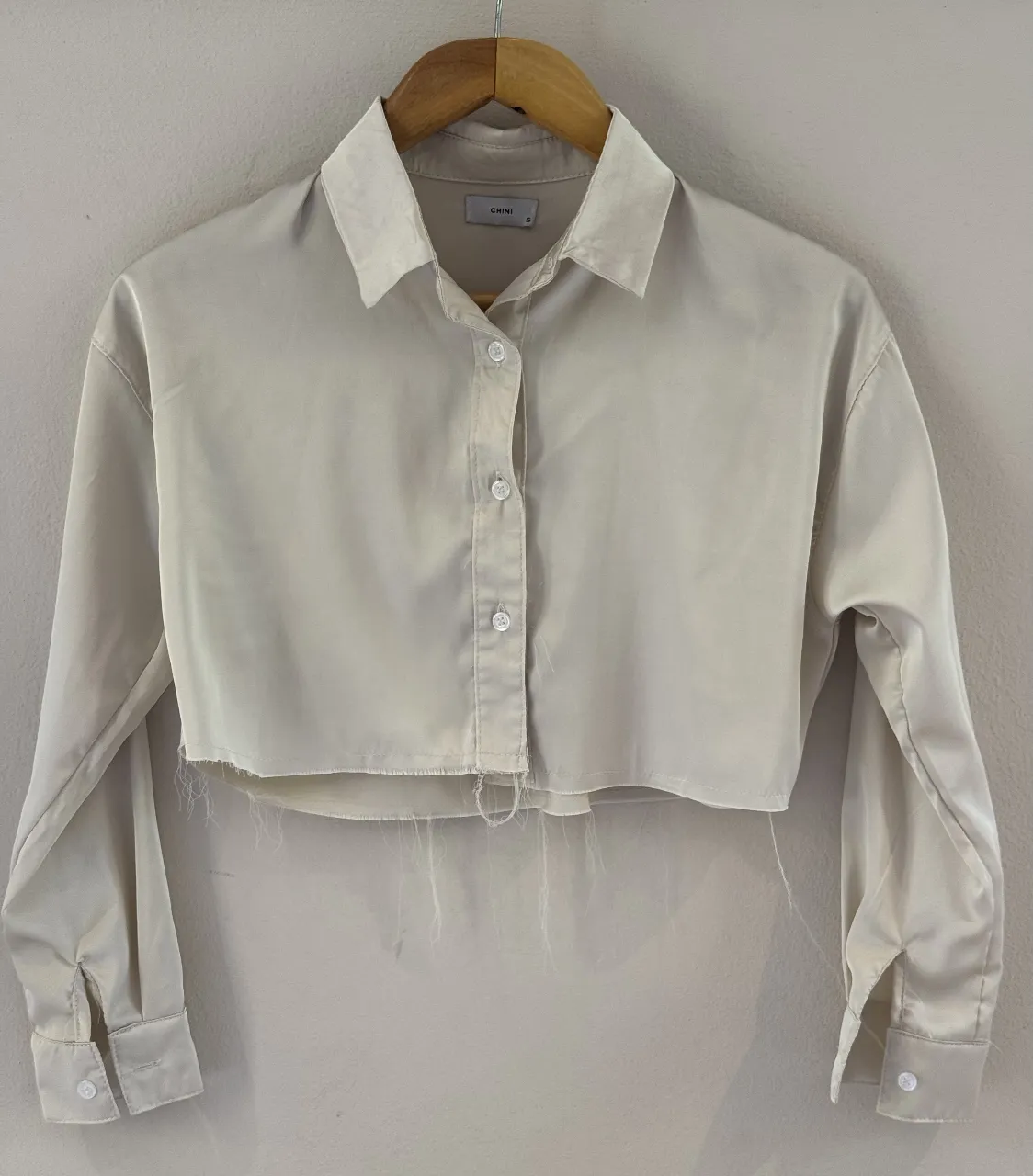 Camisa crop de seda color crudo, con botones al frente y terminación desflecada. Ideal para un look canchero y moderno.