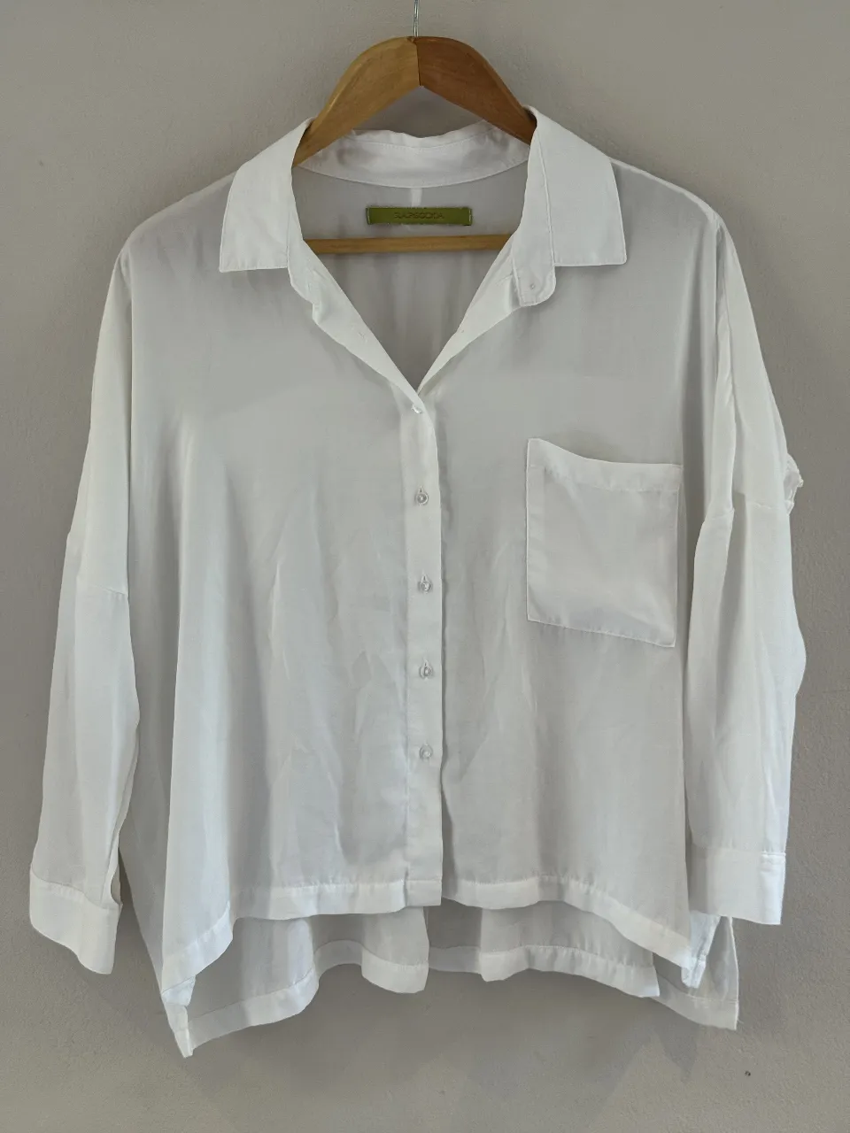 Camisa blanca de seda, con mangas largas y detalles de volados en la espalda. Posee un bolsillo en el frente y botones nacarados. Perfecta para un look elegante y sofisticado.