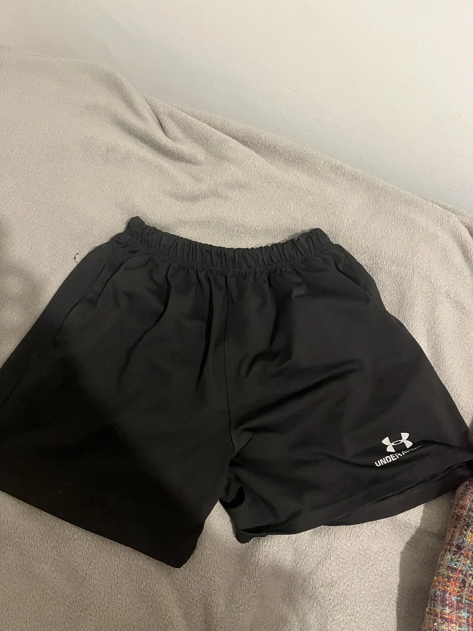 Short deportivo negro de hombre, ideal para entrenar o usar en el día a día. Con logo de la marca Under Armour en blanco.
