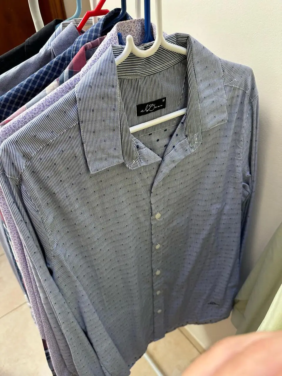 Camisa a rayas celeste y blanca de hombre, con detalles de puntos en la tela. Cuello con detalles en negro y etiqueta de la marca.