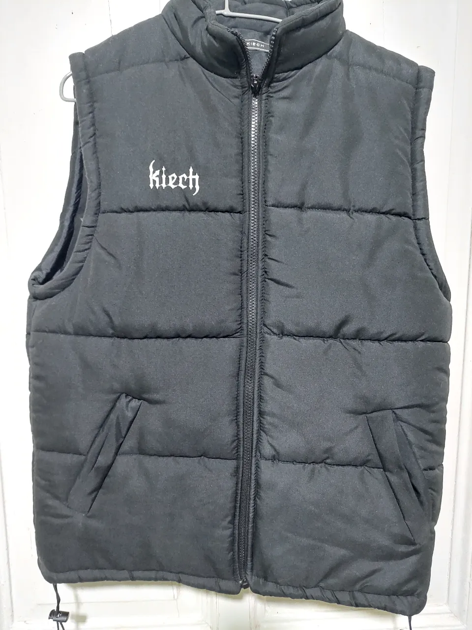 Chaleco negro acolchado con cierre frontal y bolsillos. Diseño con logo "Kiech" en el pecho y detalles "ARG. BUENOS AIRES" en la espalda. Ideal para un look urbano y abrigado.