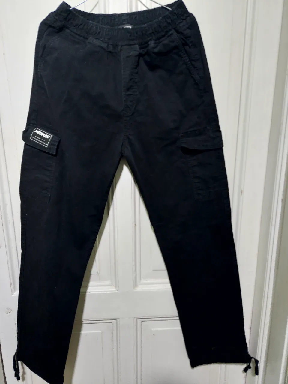 Pantalón cargo negro de hombre, con bolsillos laterales y etiqueta de la marca Midway. Ideal para un look casual y urbano.