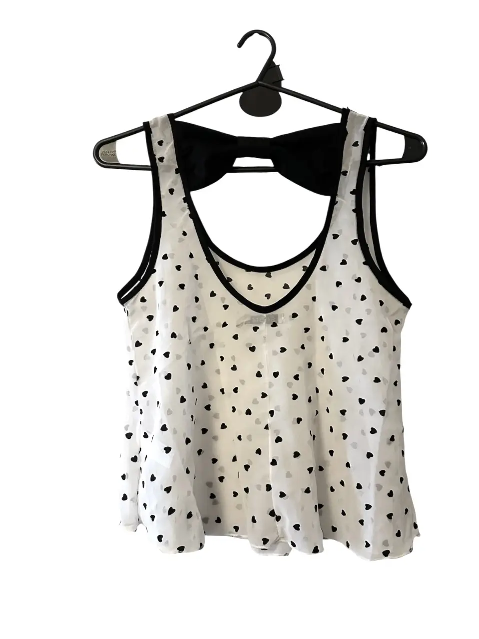 Top blanco con estampado de corazones negros y detalle de moño en la espalda. Ideal para un look casual y femenino.