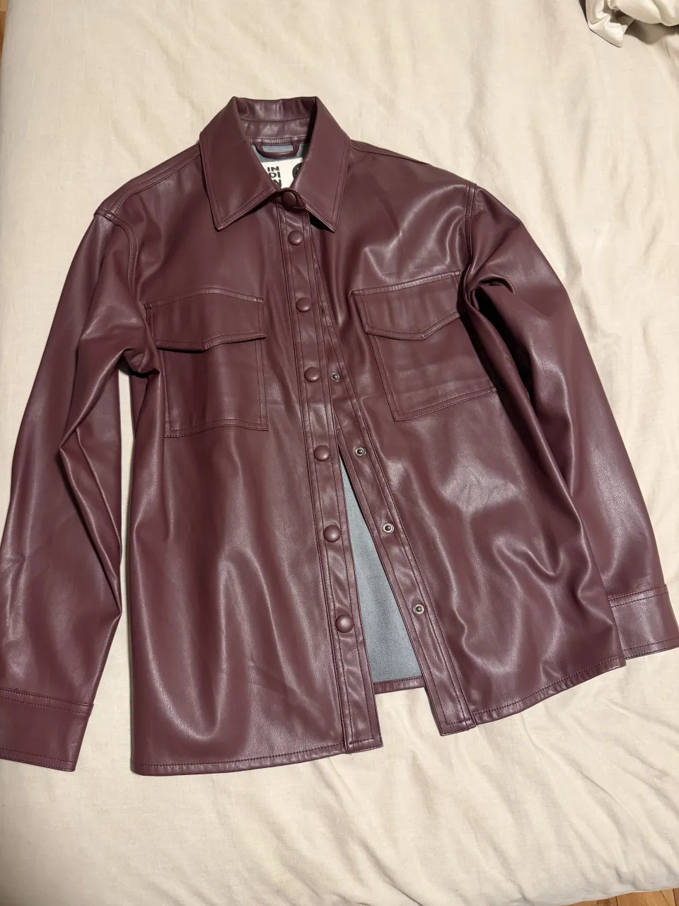 Camisa de cuero sintético color bordó con botones al frente y dos bolsillos en el pecho.