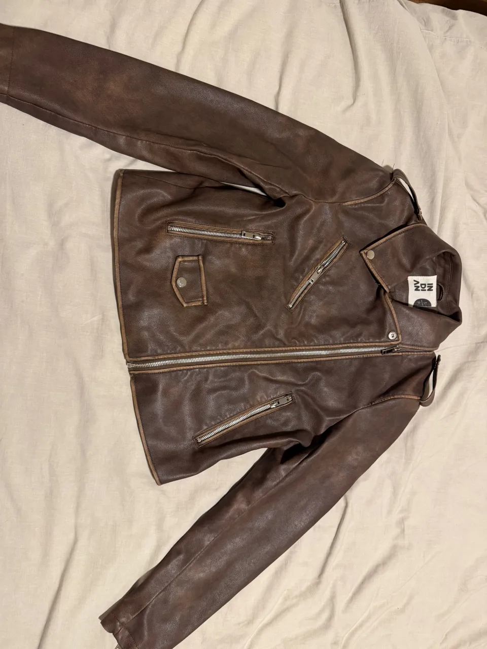 Campera de cuero marrón con cierres metálicos y detalles de costura. Tiene cuello con solapa y un bolsillo con tapa en el frente.