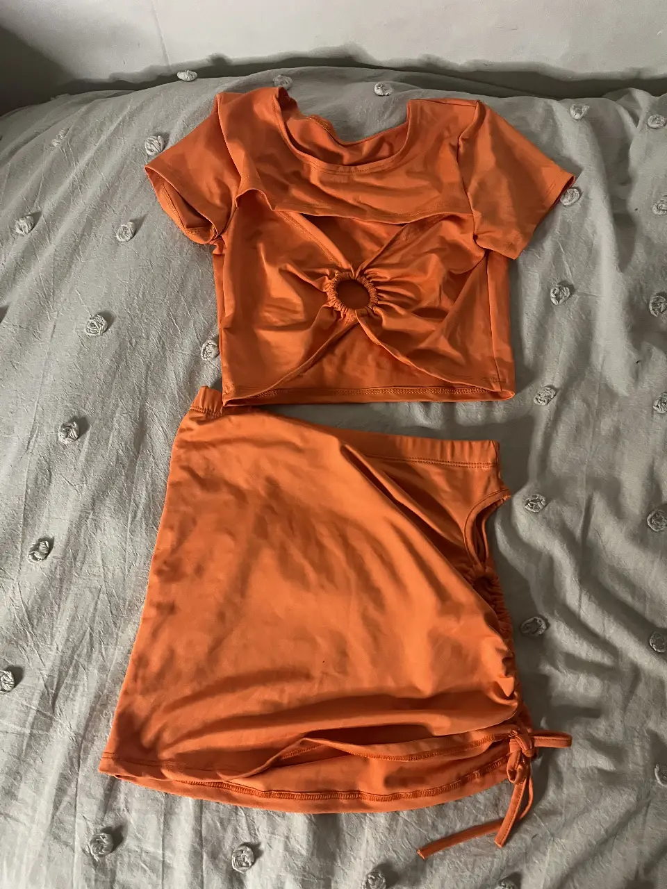 Conjunto naranja de dos piezas, top con detalle de aro en el centro y falda con ajuste lateral. Ideal para un look moderno y fresco.