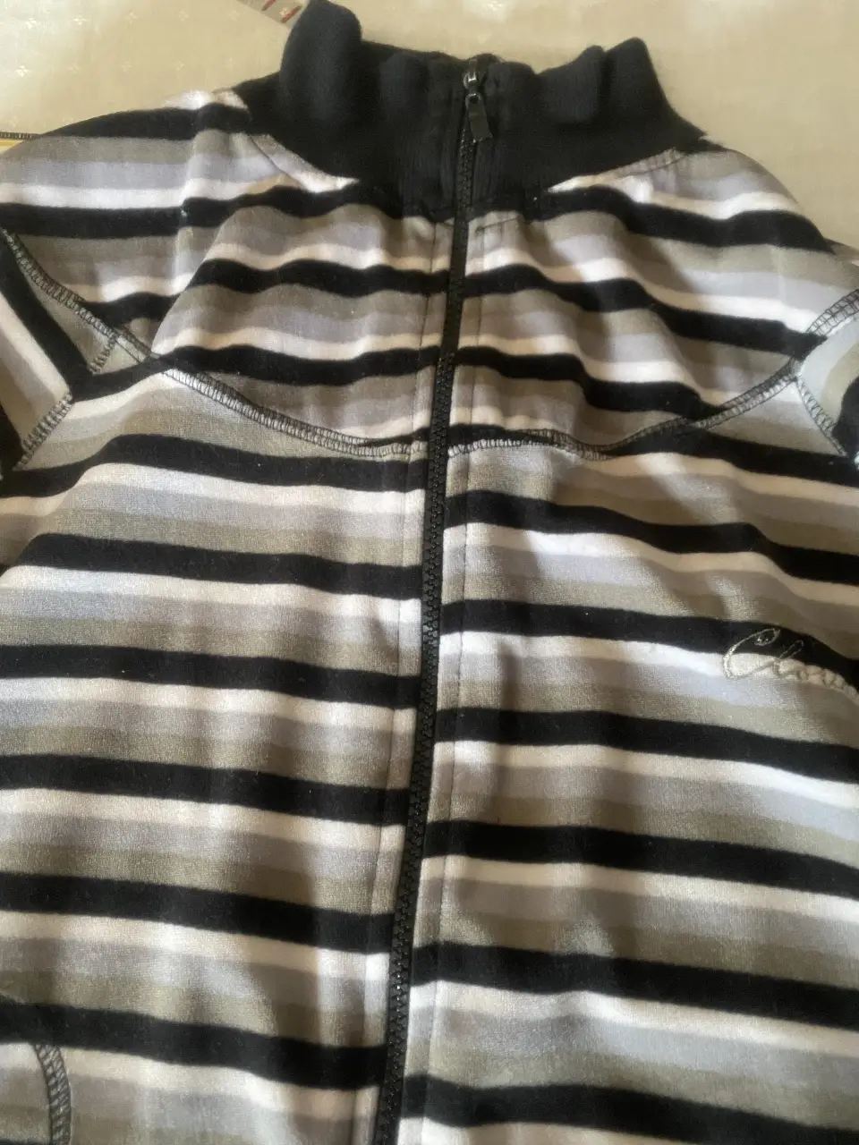 Buzo con cierre a rayas horizontales en tonos grises y negro. Cuello alto y puños en color negro. Ideal para un look casual y abrigado.