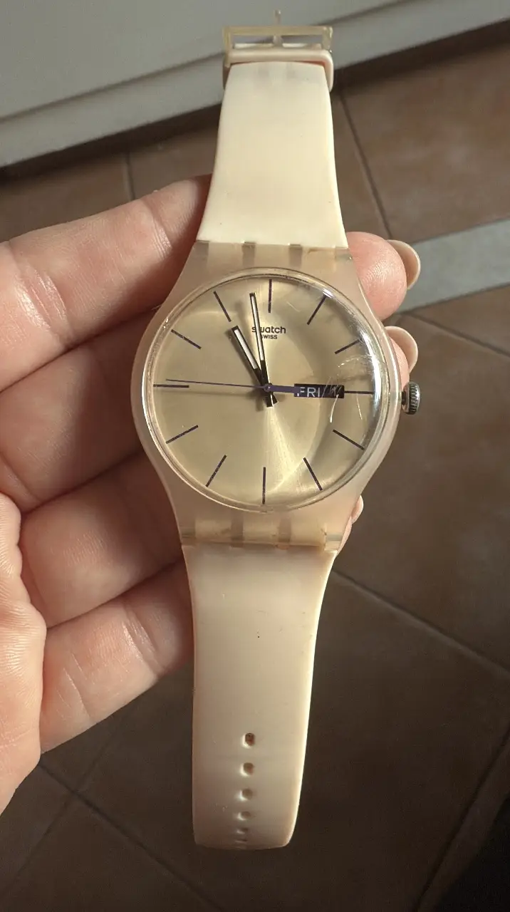 Reloj Swatch de plástico color crema con esfera dorada y detalles en negro. Diseño clásico y funcional, ideal para uso diario.