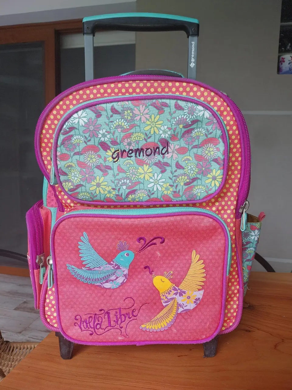 Mochila Gremond con carrito, ideal para llevar libros y útiles escolares. Diseño colorido con detalles de flores y aves. Perfecta para estudiantes.