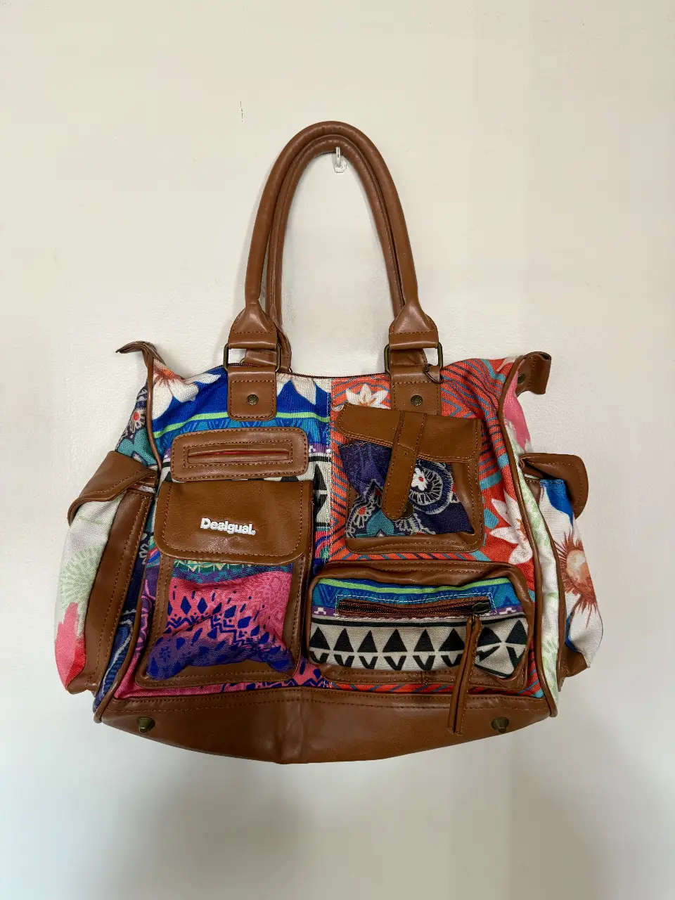 Cartera Desigual con diseño patchwork, múltiples bolsillos y detalles en cuero marrón. Ideal para un look bohemio y casual.
