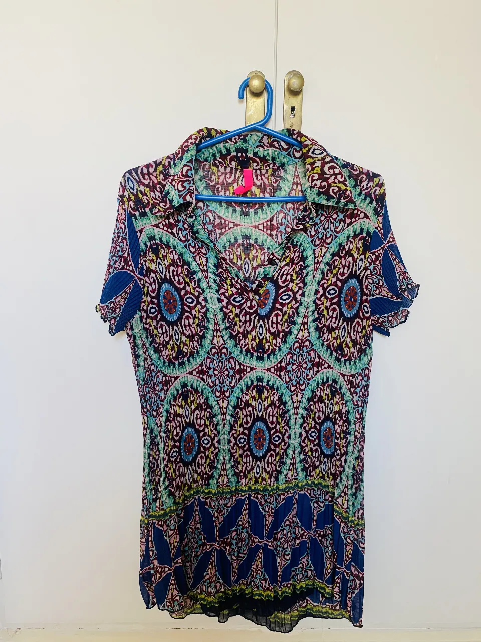 Blusa estampada con diseño floral en tonos turquesa, rosa y azul. Plisada y larga. Corte holgado y mangas cortas. Ideal para un look fresco y femenino.