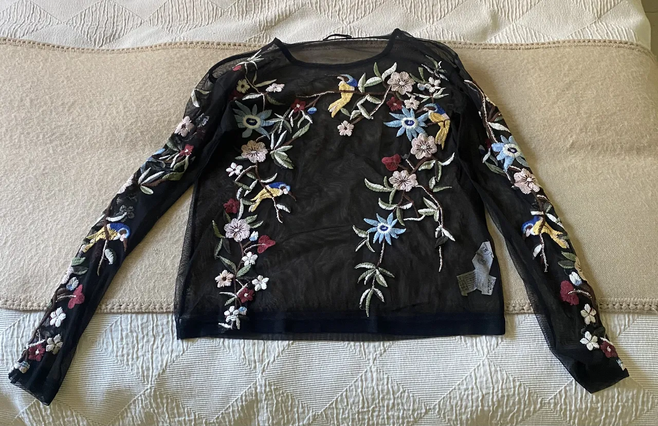 Blusa de tul negra con bordados florales y aves. Tiene sosndex. Ideal para un look elegante y sofisticado. Perfecta para combinar con jeans o pantalones de vestir.