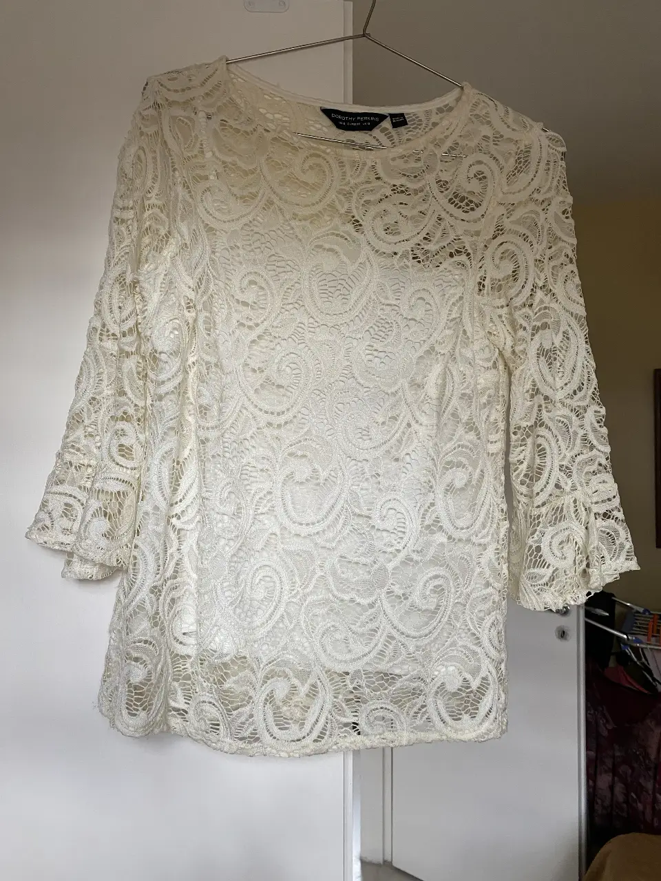 Blusa de encaje elastizado blanca de la marca Dorothy Perkins, con mangas 3/4 y cuello redondo. Ideal para un look elegante y femenino.