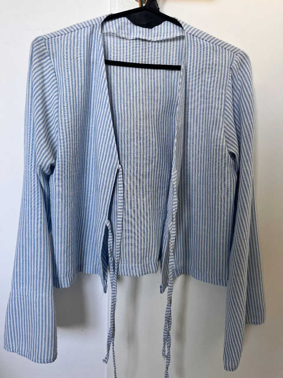 Blusa a rayas celeste y blanca, con mangas largas y lazos para atar en la cintura. Ideal para un look casual y fresco.