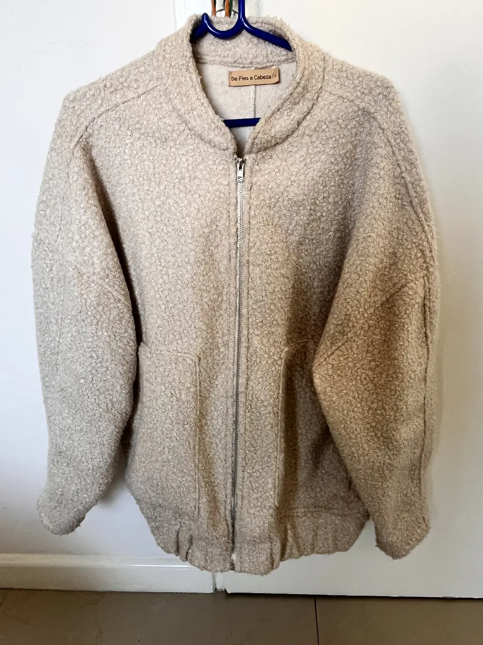 Campera bomber de tela tipo borrega en color crudo, con cierre frontal y bolsillos. Ideal para un look casual y abrigado.