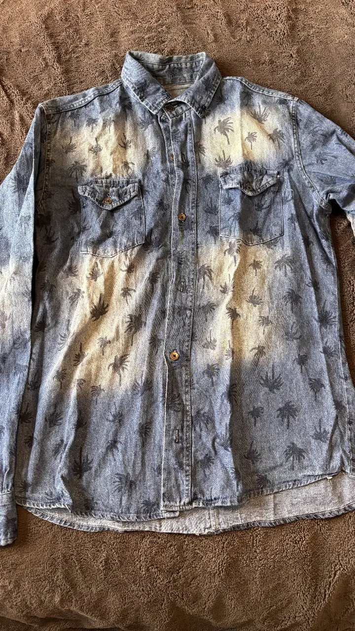 Camisa de hombre de jean con estampado de palmeras. Ideal para un look casual y playero. Corte clásico con dos bolsillos delanteros.