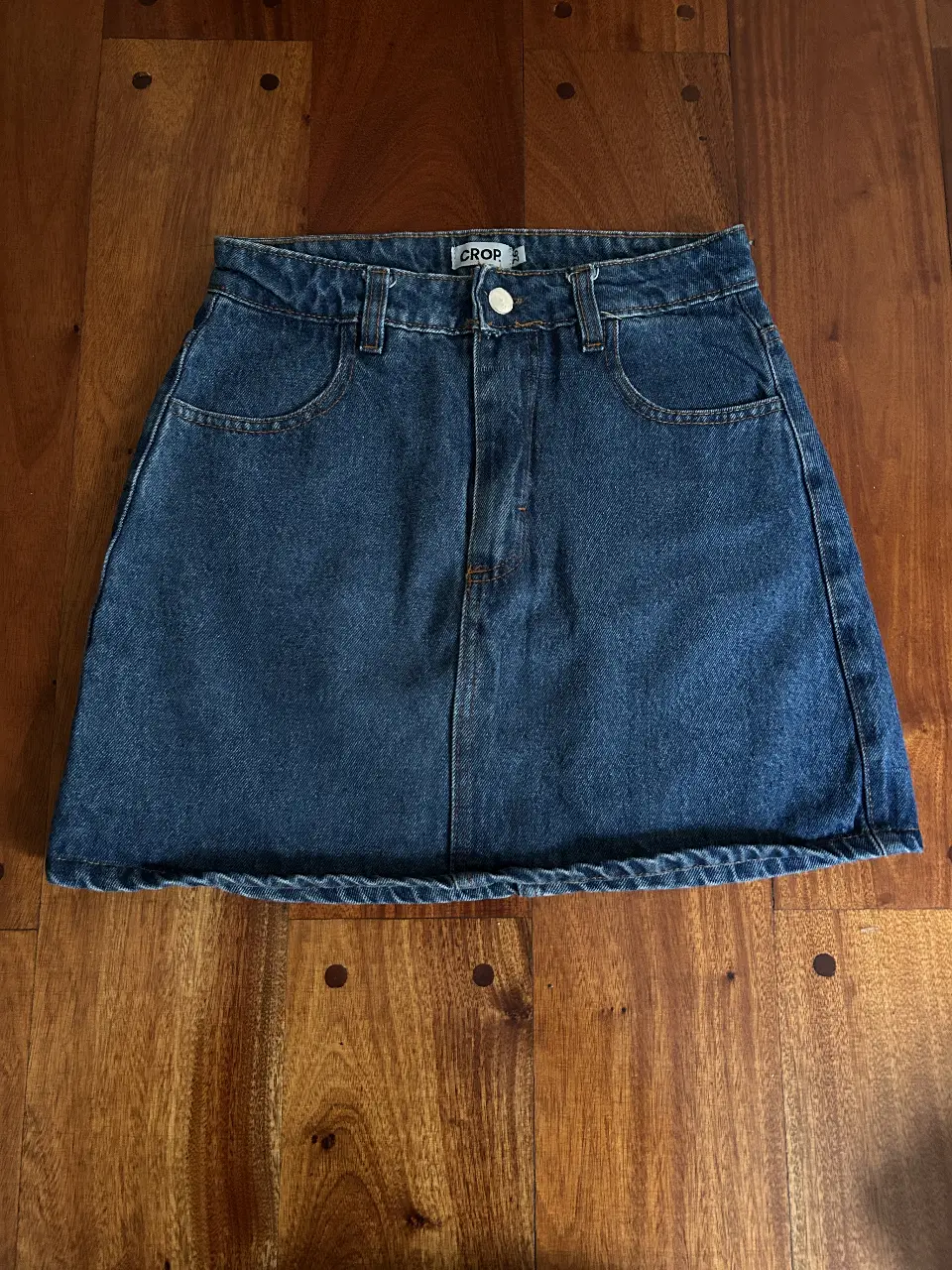 Minifalda CROP de jean azul, tiro medio, con bolsillos delanteros y traseros. Ideal para un look casual y moderno.