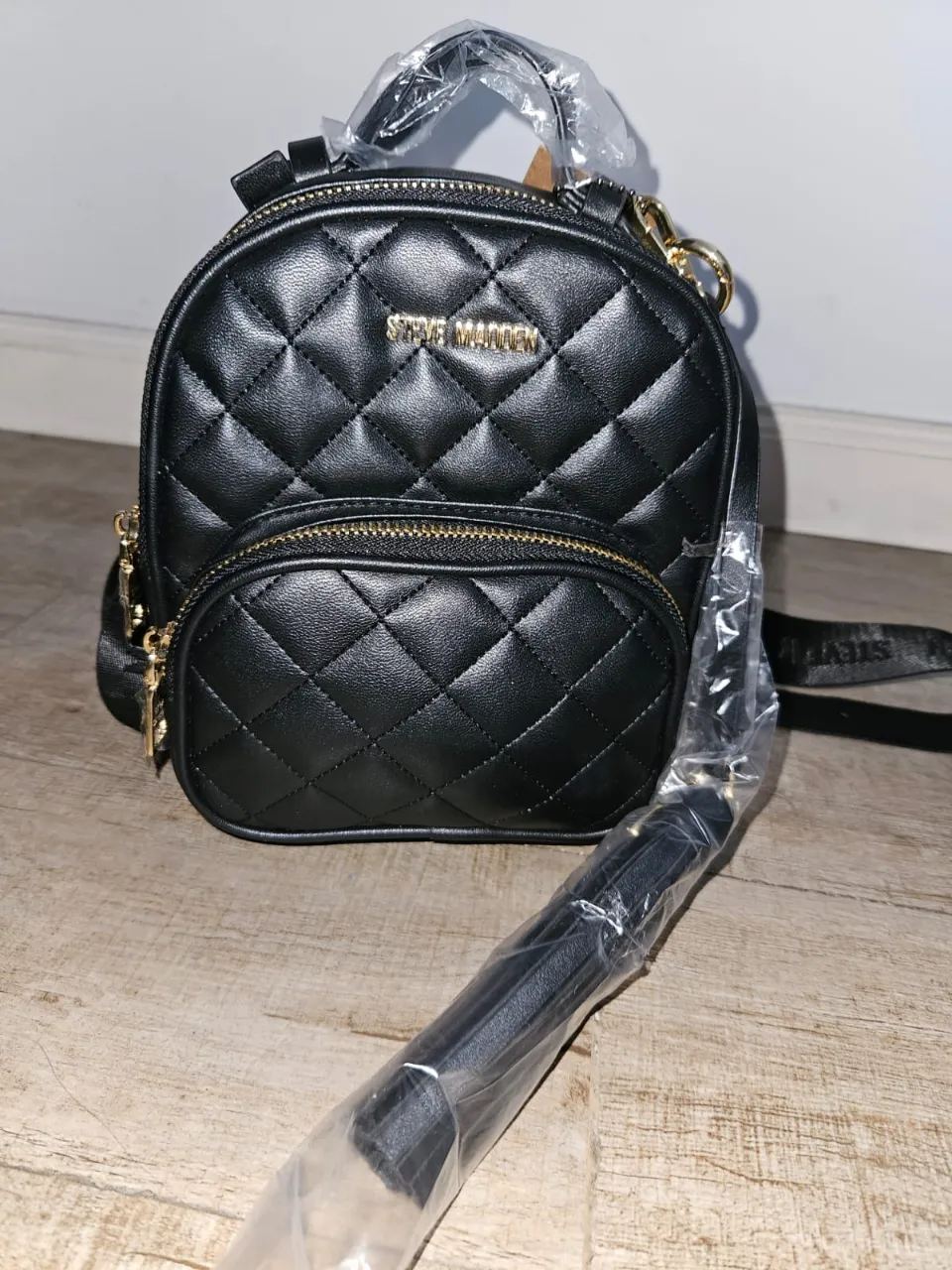 Mochila "Steve Madden" pequeña, negra acolchada, súper práctica y canchera. Viene con un monedero/tarjetero y un detalle de flecos, ideal para darle un toque chic a tu look. Perfecta para el día a día o una salida.