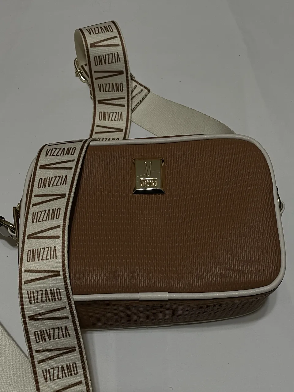 Bandolera Vizzano marrón clarito con detalles en blanco y correa con el logo de la marca. Ideal para llevar lo esencial con estilo.