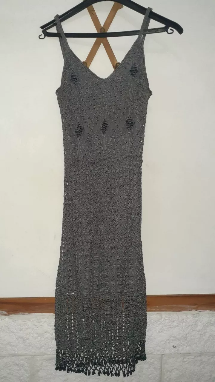 Vestido largo de crochet gris, con detalles de canutillos en el busto y terminación de flecos en el ruedo. Ideal para un look boho chic o playero.