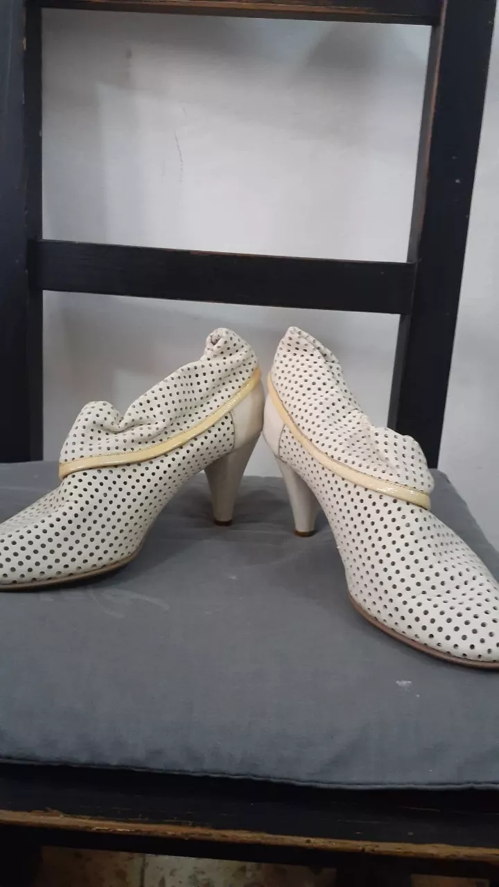 Botitas de cuero blanco con perforaciones y detalle fruncido en el cuello. Taco alto y punta fina. Ideales para un look elegante y sofisticado.