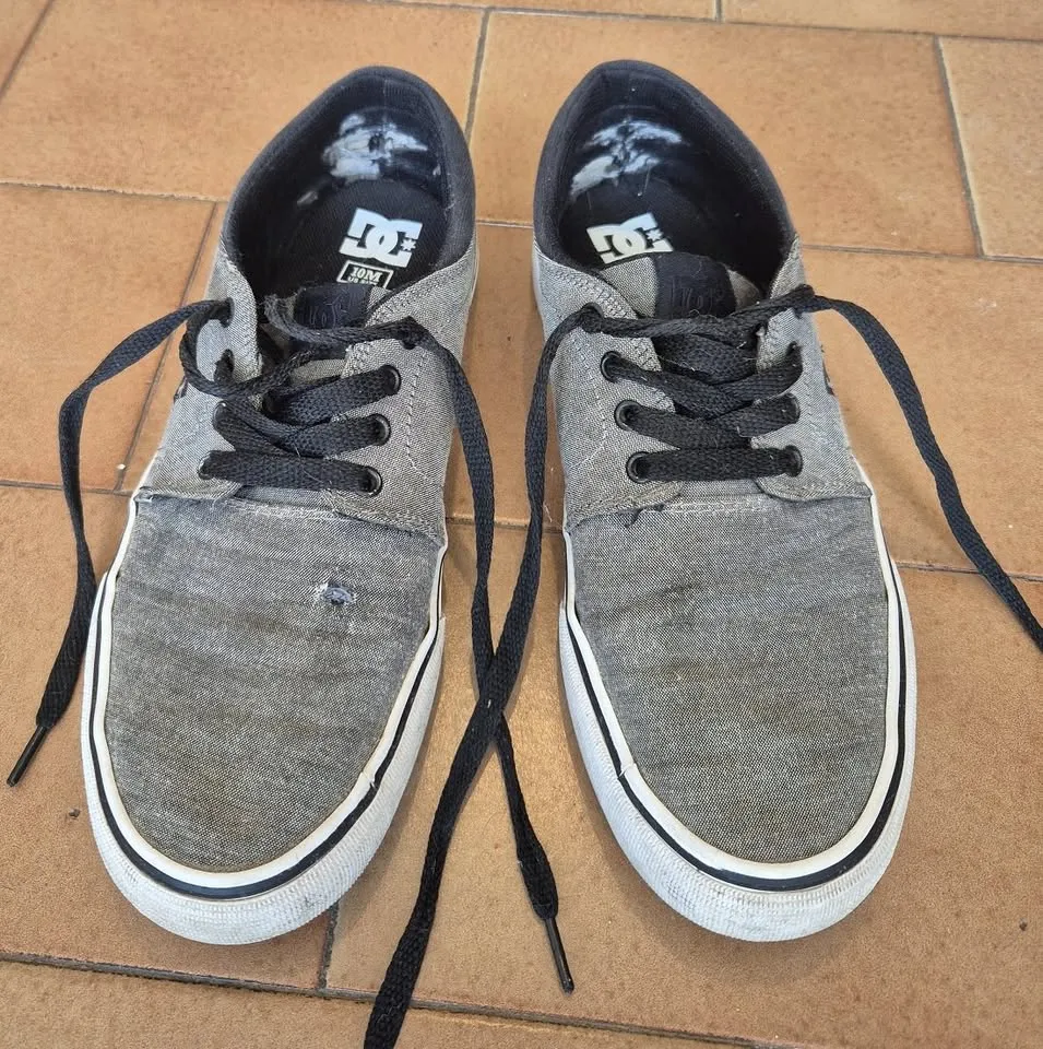 Zapatillas DC Shoes Trase Tx grises con detalles blancos y cordones negros. talle 10 o 43 (plantilla de 28cm). con detalle de reparación y costura en la derecha. Ideales para un look casual y urbano.