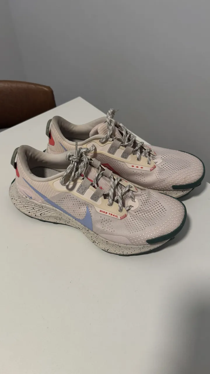 Zapatillas deportivas Nike Trail color rosa pálido con detalles en celeste y rojo. Suela verde con diseño antideslizante.