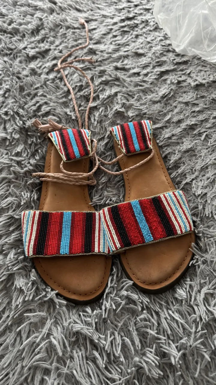 Sandalias sarkany planas de tiras con detalle de mostacillas multicolores y cordones para atar en el tobillo.