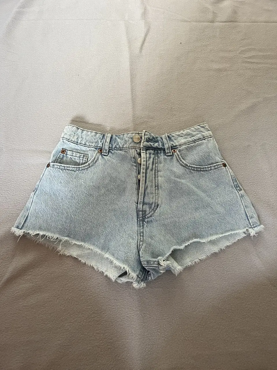 Short de jean celeste de mujer, tiro medio, con detalles de roturas en los bordes. Ideal para un look casual y moderno.