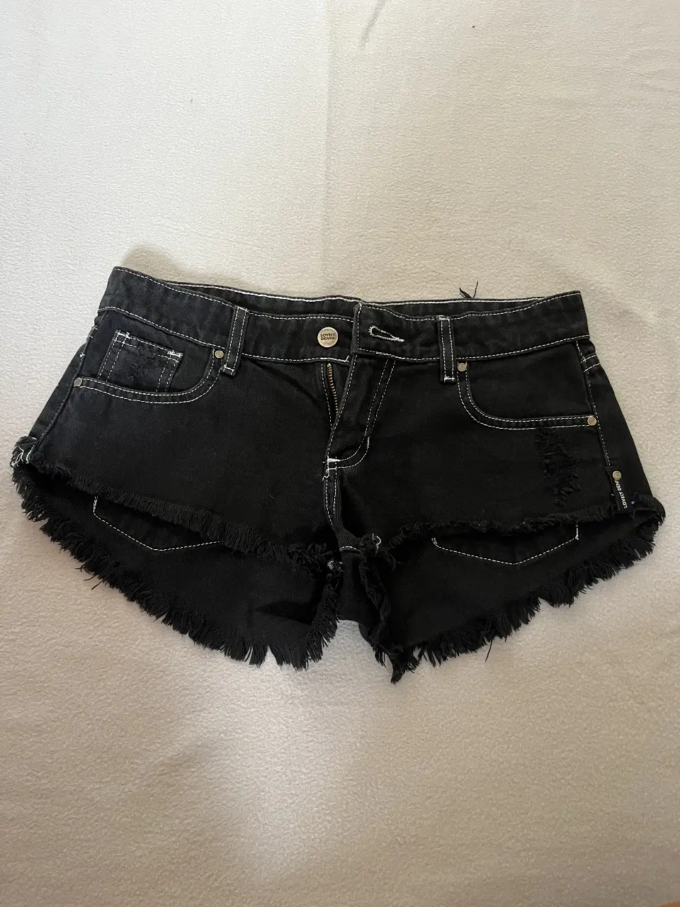 Short de jean negro con detalles de roturas y flecos en el borde. Tiro bajo. Talle 26, ideal para un look casual y moderno.
