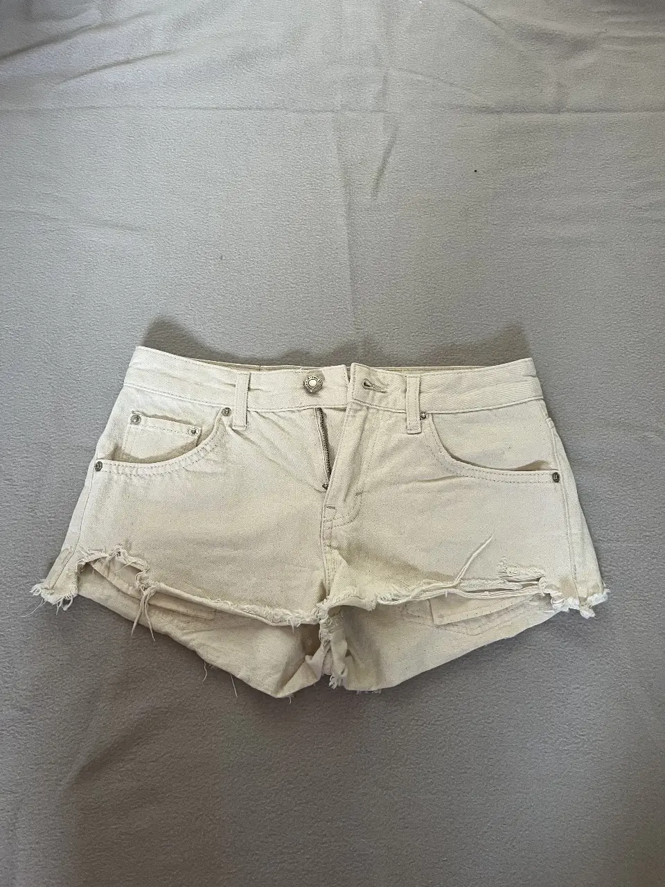 Short de jean tiro bajo en color crudo, con detalles de roturas en los bordes. Ideal para un look casual y fresco.