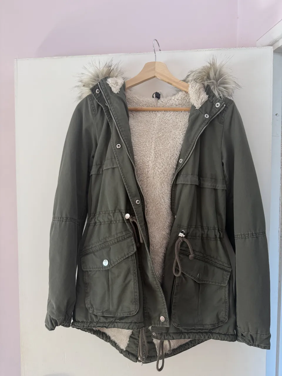 Parka verde militar con forro interno de corderito súper abrigado y capucha con piel sintética. Ideal para los días más fríos del invierno. Tiene bolsillos amplios y cordón ajustable en la cintura para un mejor calce.