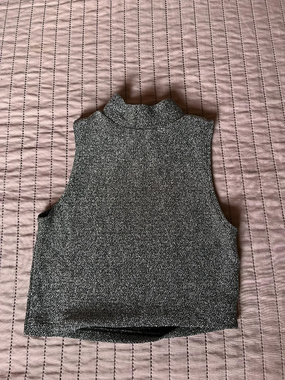 Top sin mangas de cuello alto, tejido con textura brillante en color gris. Ideal para un look moderno y sofisticado.