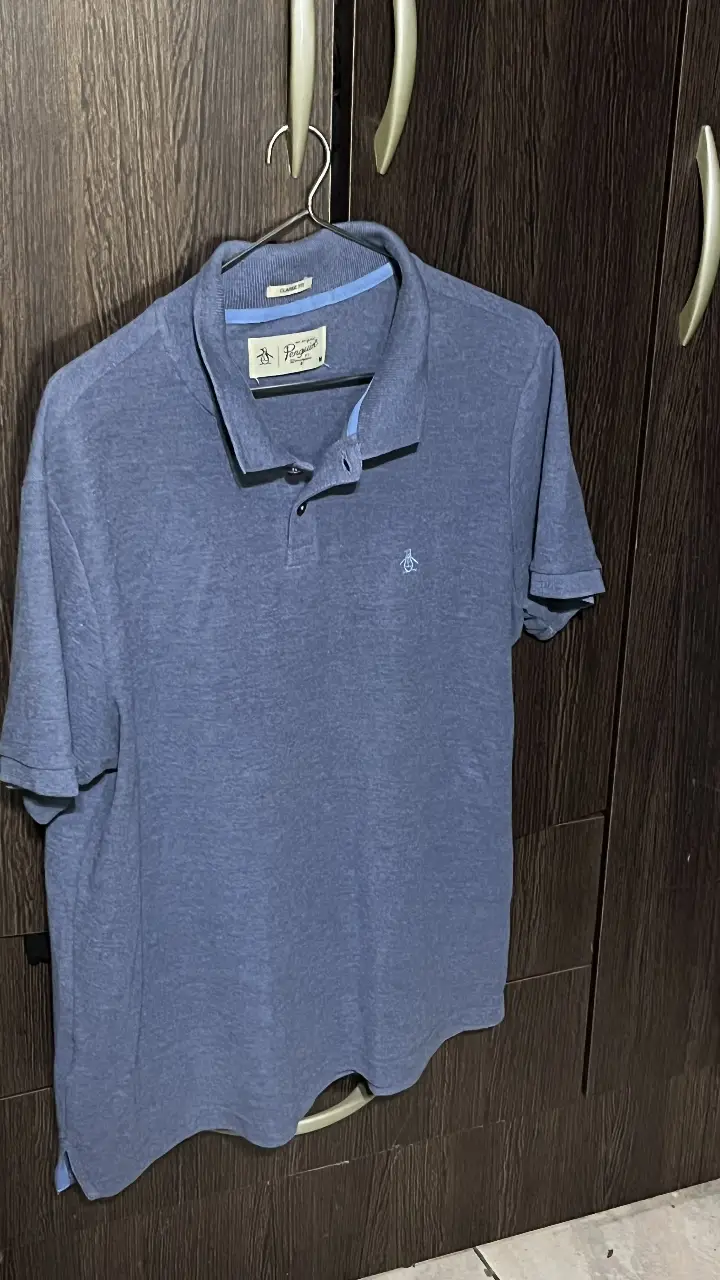 Remera tipo polo de hombre, color azul, de la marca Original Penguin. Confeccionada en tela suave y cómoda, ideal para un look casual y elegante. Cuello con botones y el logo del pingüino bordado en el pecho.