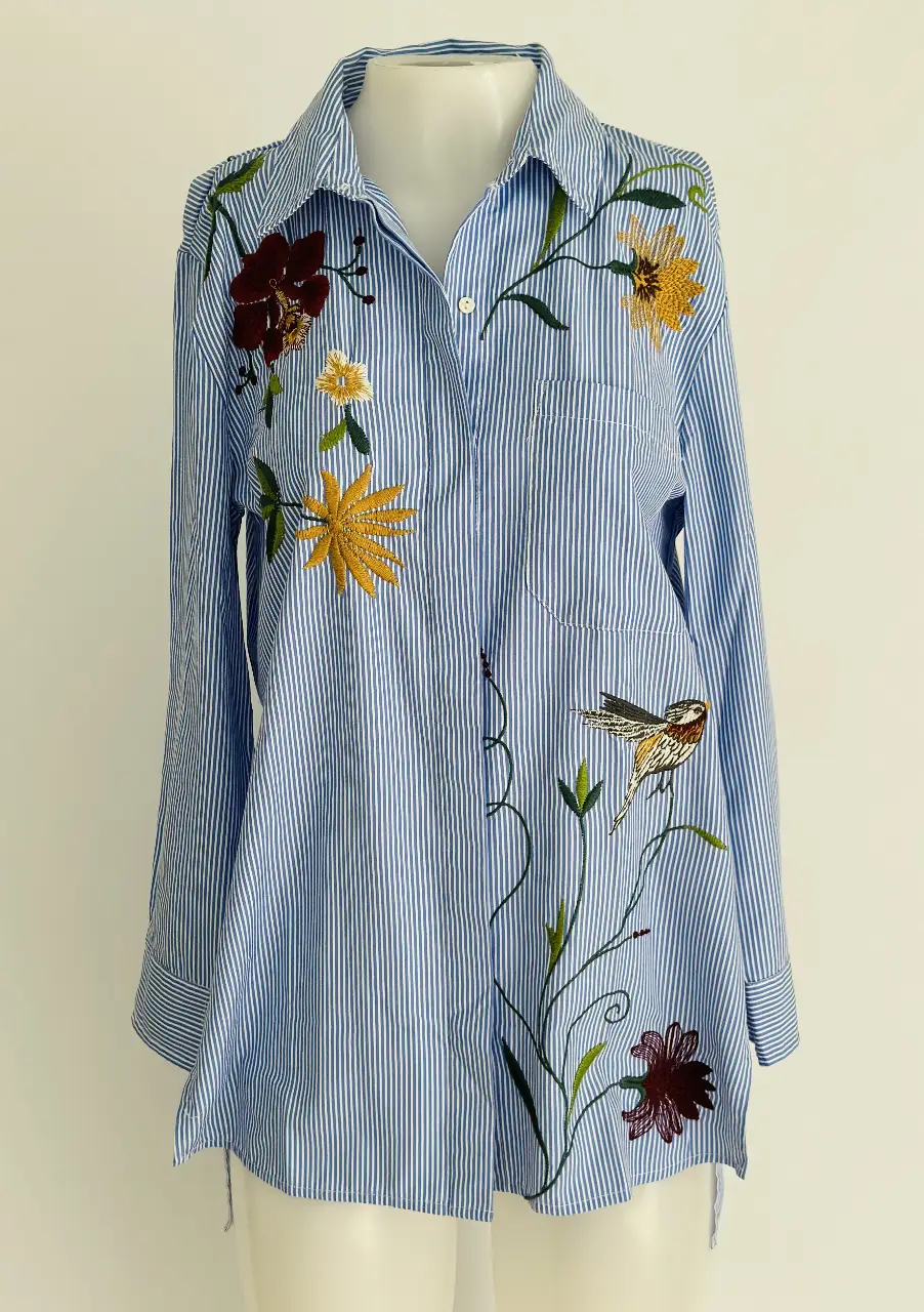 Camisa de mujer a rayas celeste y blanca con bordados florales y de pájaros. Diseño artesanal y detalles únicos.