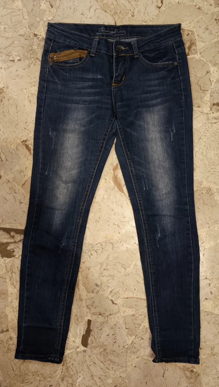 Jeans de mujer, corte recto, con detalles de desgaste y un bolsillo con cierre dorado. Diseño con detalles en los bolsillos traseros.
