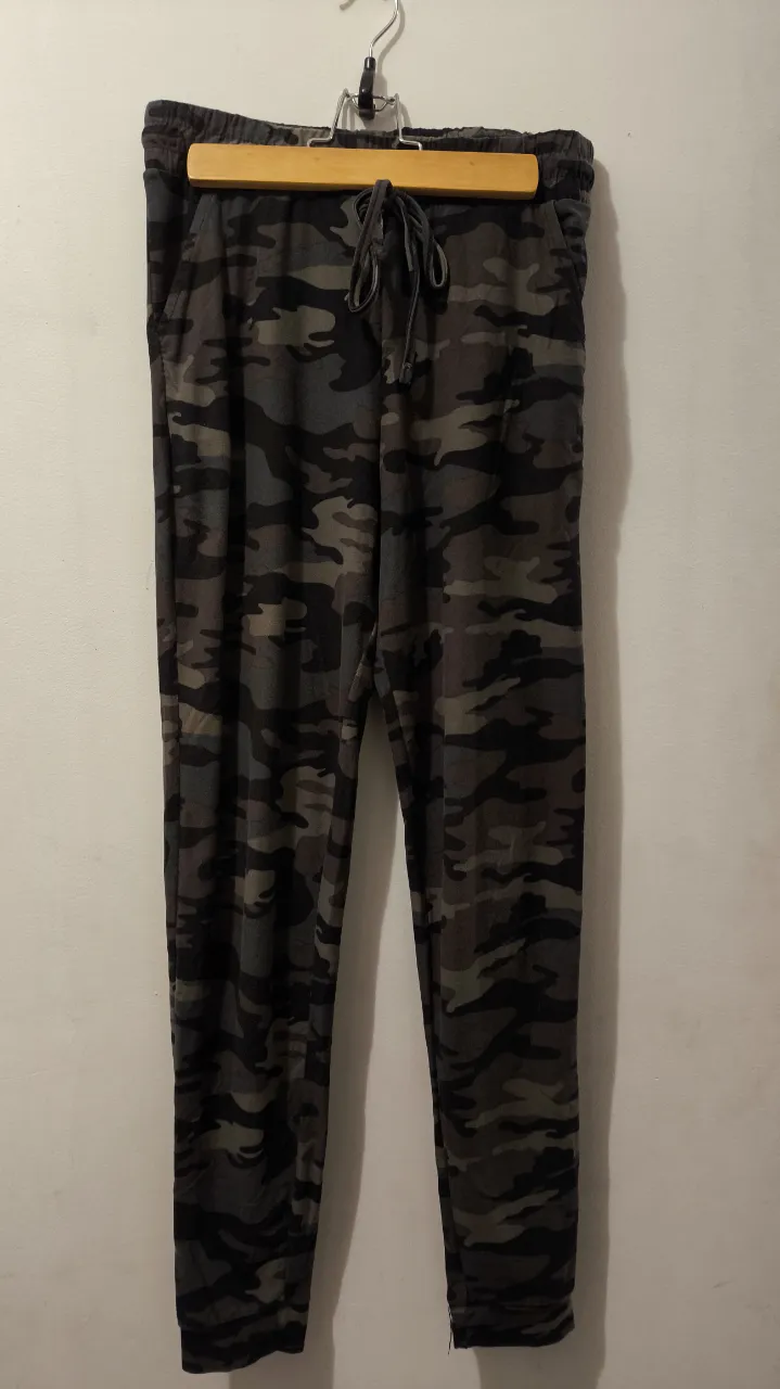Pantalón de hombre con estampado camuflado en tonos grises y marrones. Tiro medio, con cintura elastizada y cordón para ajustar. Bolsillos laterales y cierre en los tobillos. Ideal para un look casual y cómodo.