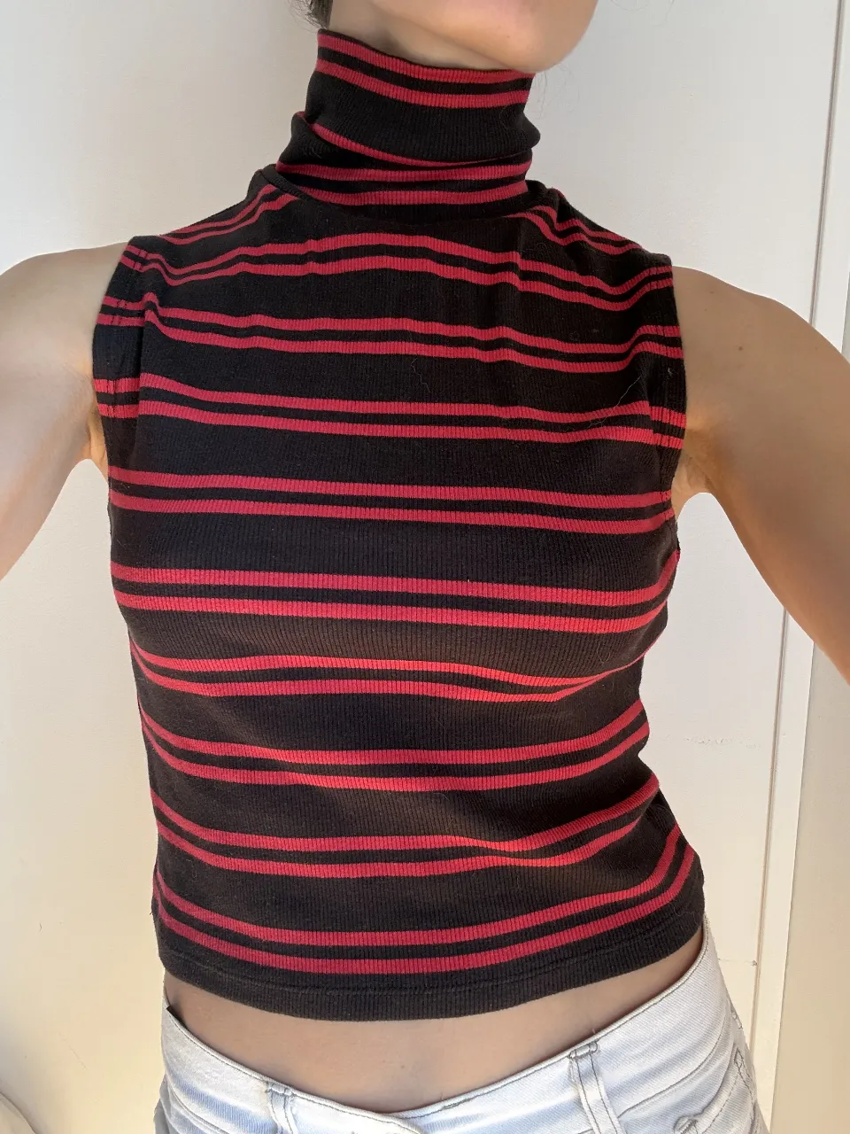 Remera de cuello alto sin mangas, con rayas verticales rojas y negras. Ideal para un look casual y moderno.